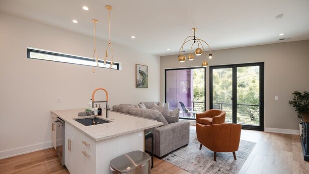A modern kitchen with a built-in island, a dining area with a grey sofa, and a large sliding glass door leading to a balcony. - Turf ROOFTOP w Games and more in Heart of Wilmington! Rent Multiple or One Unit! Unit C (Wilmington)