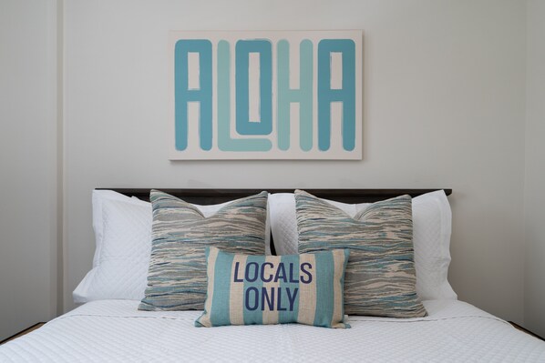 Ein Bett mit weißer Bettwäsche und zwei Kissen, eines mit dem Aufdruck 'Locals Only'.