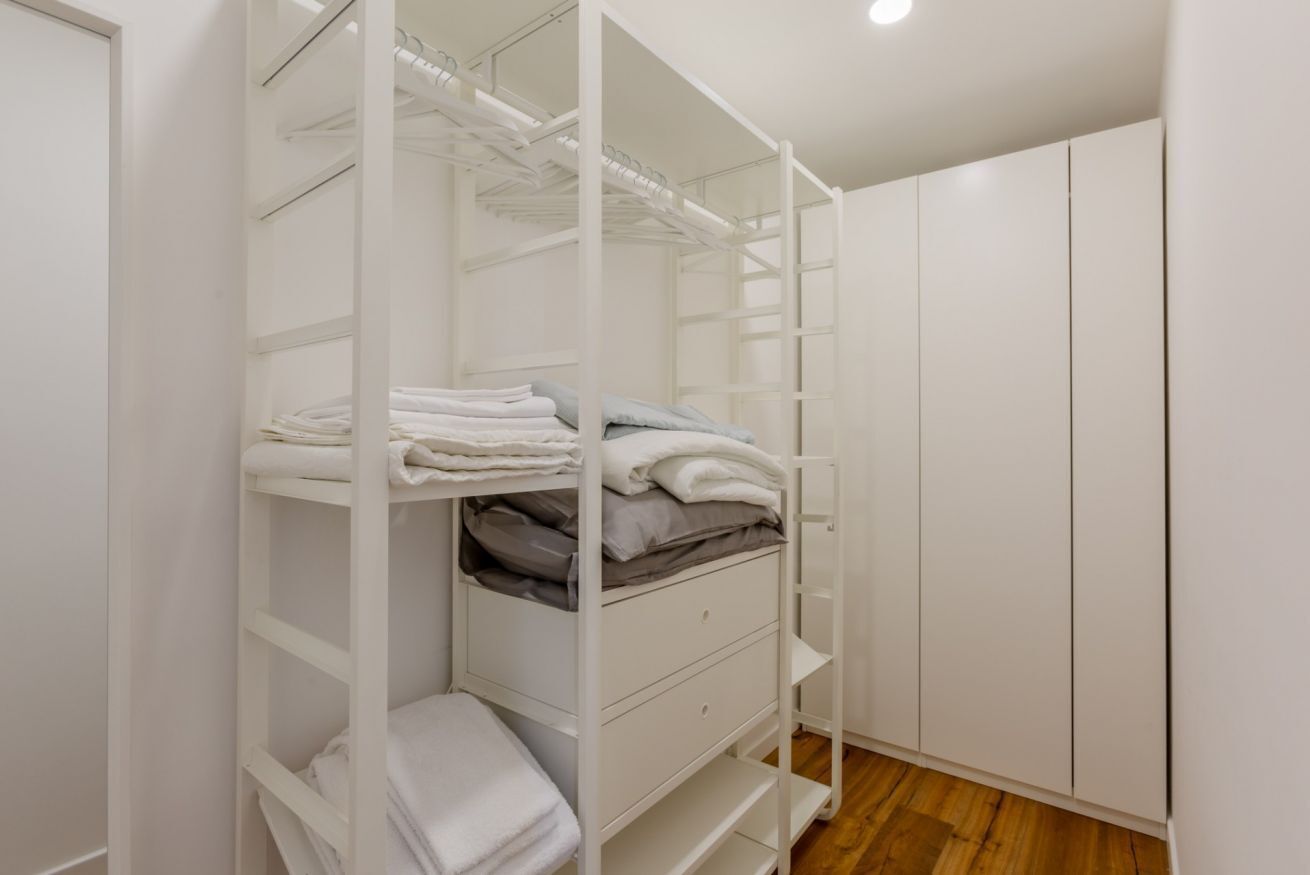 Ein weißer Kleiderschrank mit Regalen und Schubladen, Holzboden und einer weißen Tür.