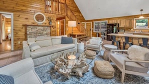 A spacious loft-style living area with a high ceiling, wooden beams, a stone fireplace, a glass coffee table, and a kitchen with a large window. - 3 Bedrooms, 1 Flex Room, 4 Bathrooms!  Come Visit 'Lake-A-Licious'! (Huddleston)