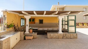 An outdoor patio with a covered seating area, stone benches, and potted plants. - Large seaside apartment with patio (Lu Bagnu)