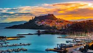 A coastal town with a historic fort on a hill, colorful buildings, and a marina with boats. - Large seaside apartment with patio (Lu Bagnu)