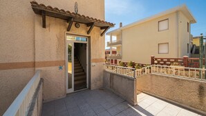 A building with a tiled entrance, a staircase leading to a balcony, and a clear sky. - Large seaside apartment with patio (Lu Bagnu)