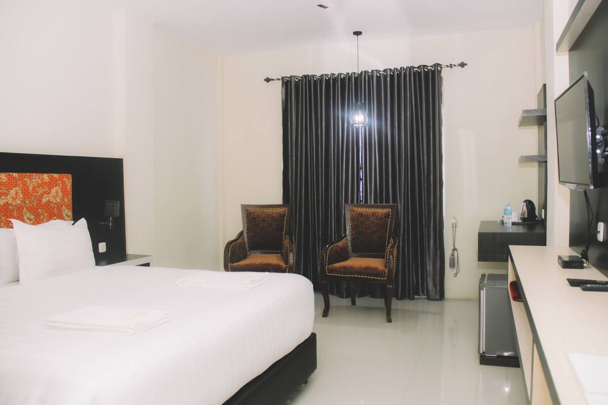 Una habitación de hotel con una cama grande, dos sillones, un escritorio y un televisor, y una cortina.