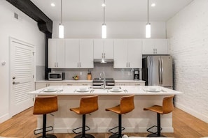 A modern kitchen with white cabinets, a central island with bar stools, stainless steel appliances, and pendant lighting.