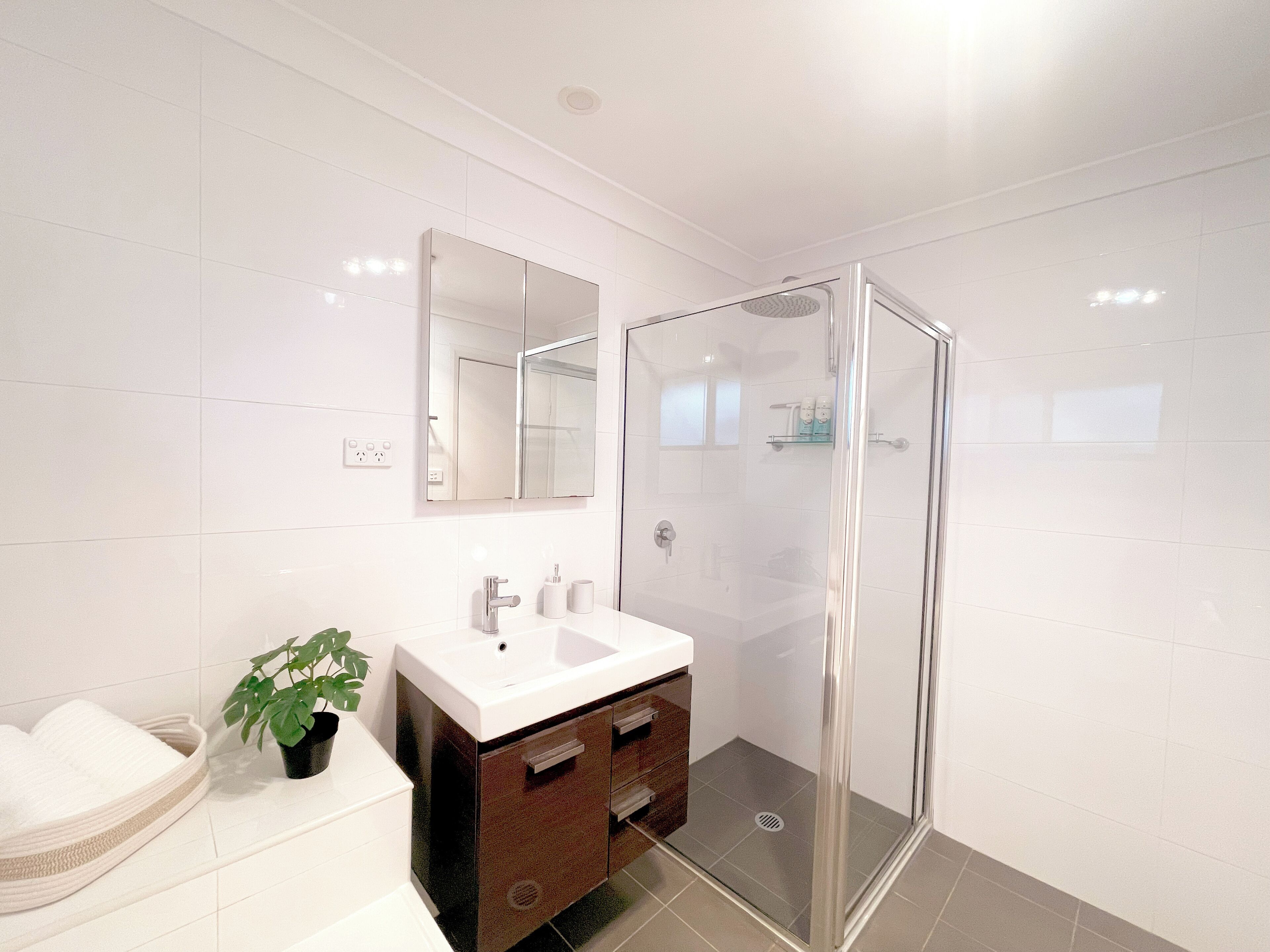 A modern bathroom with a glass-enclosed shower, a white sink, and a mirror above it.