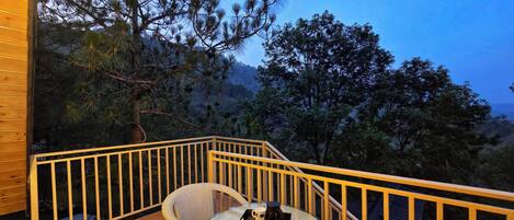 A wooden deck with wicker chairs and a table, overlooking a mountainous landscape.