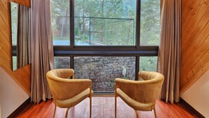 Una habitación con dos sillones, ventanas amplias y una pared de piedra.