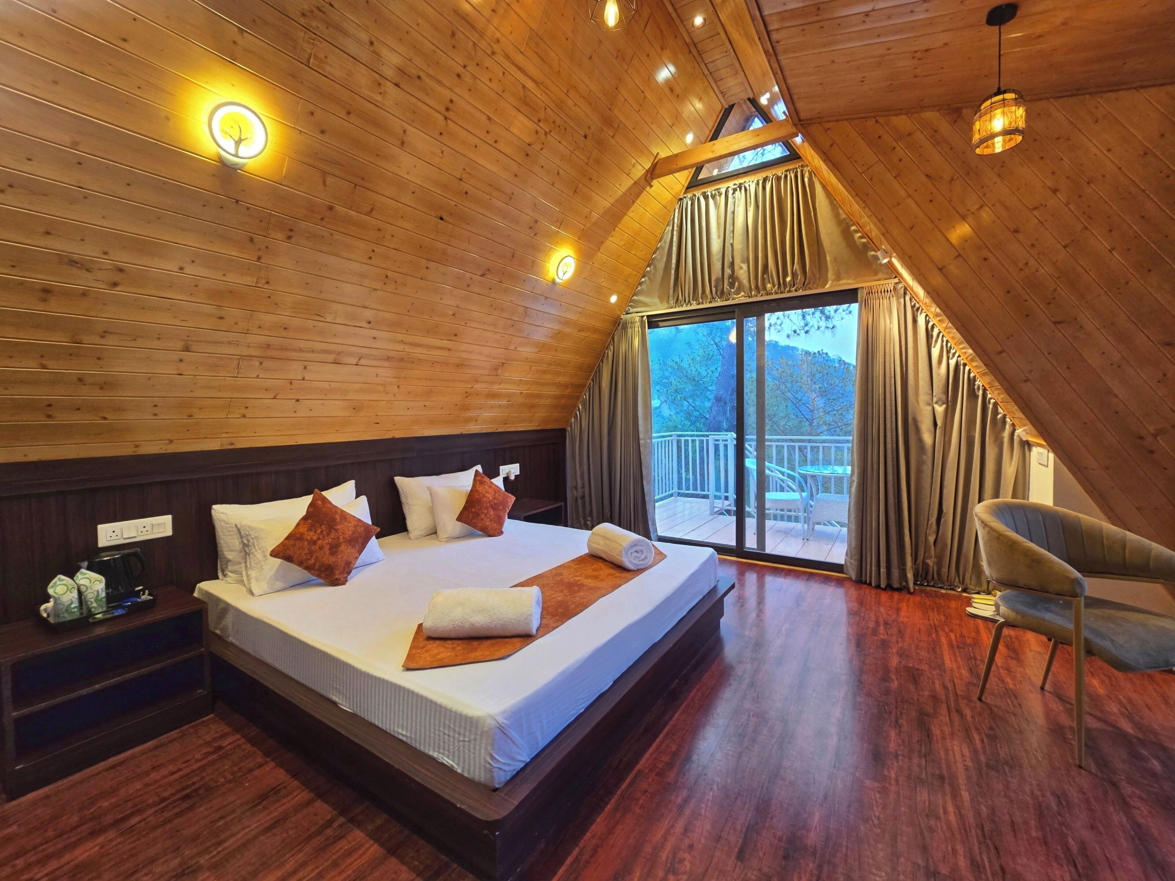 A cozy, sloped-roof bedroom with a large bed, wooden walls, and a balcony with a view.