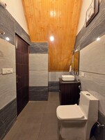 Un baño moderno con techo de madera, puerta de madera oscura, inodoro blanco, lavabo y espejo.