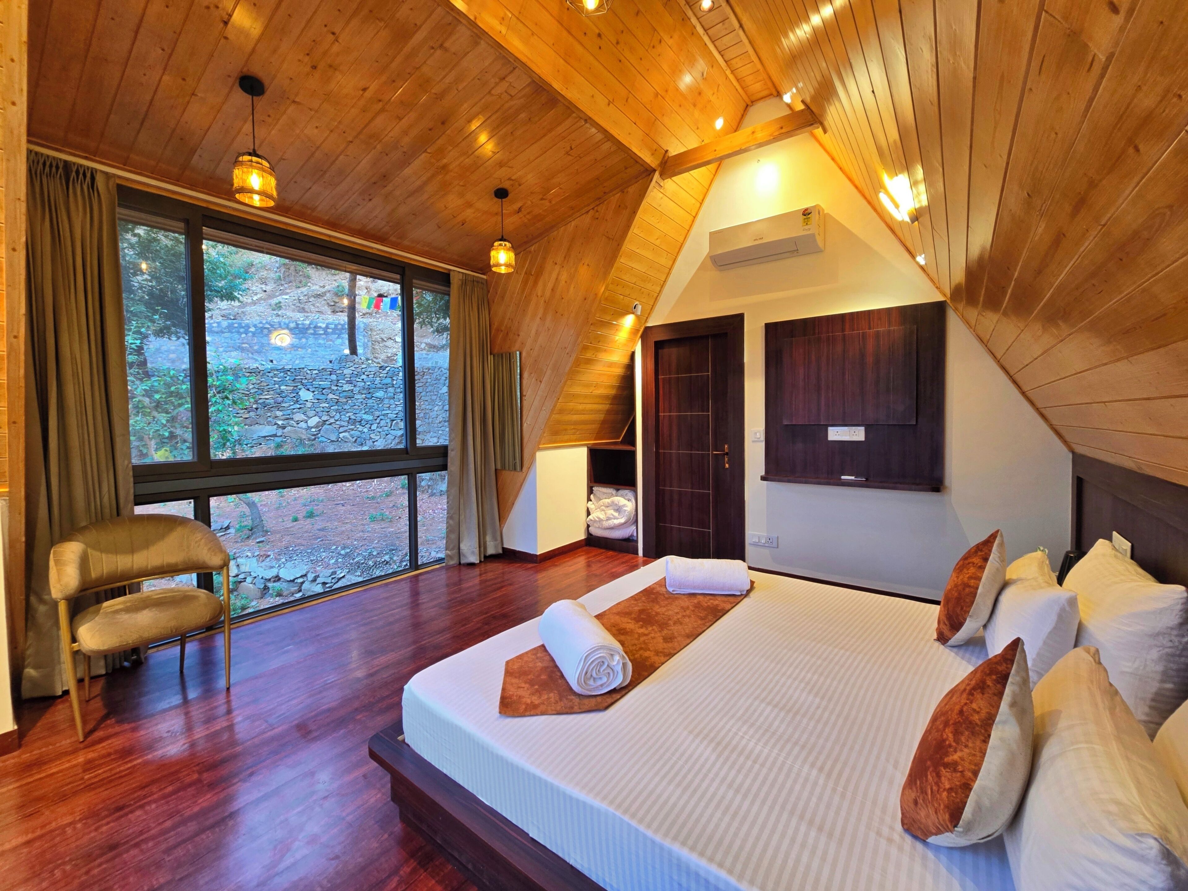 A bedroom with a large bed, wooden ceiling, and a view of the outdoors.