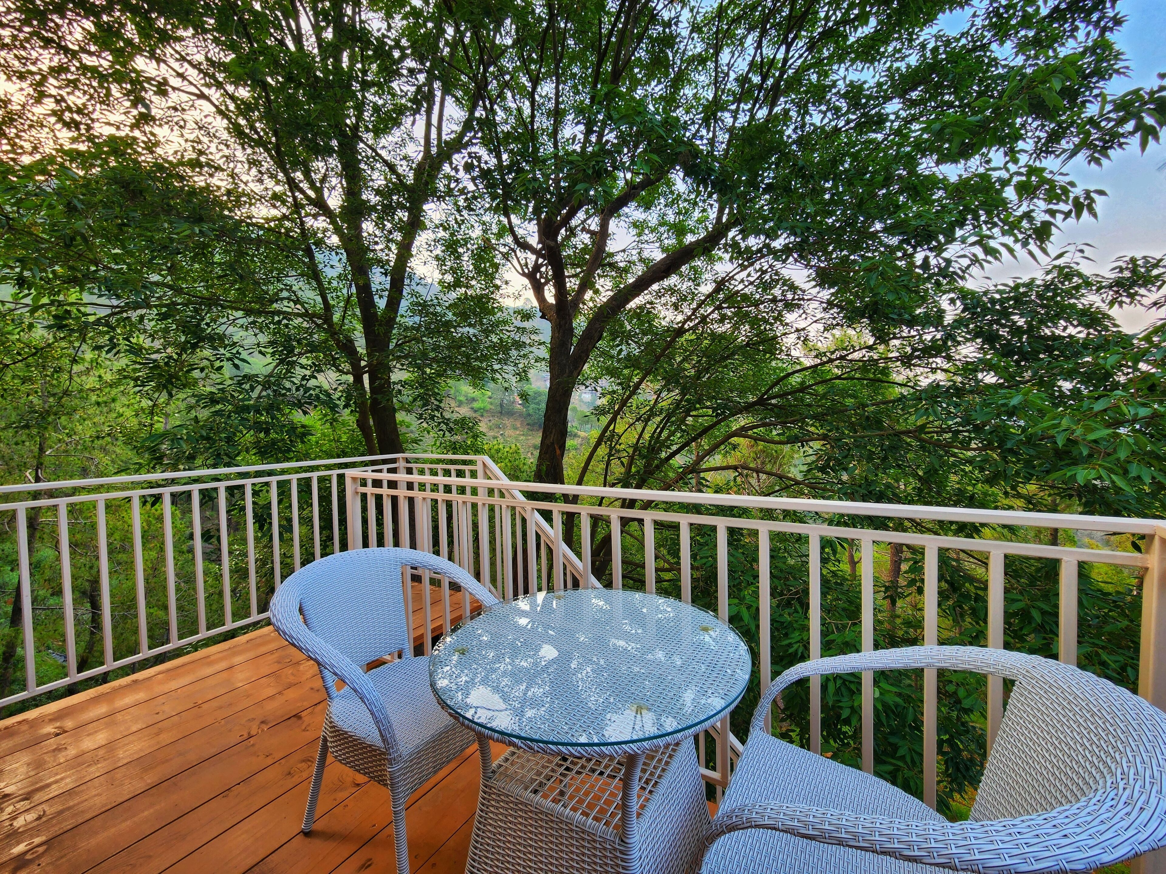 A wooden deck with wicker furniture and a railing overlooking a forested area.