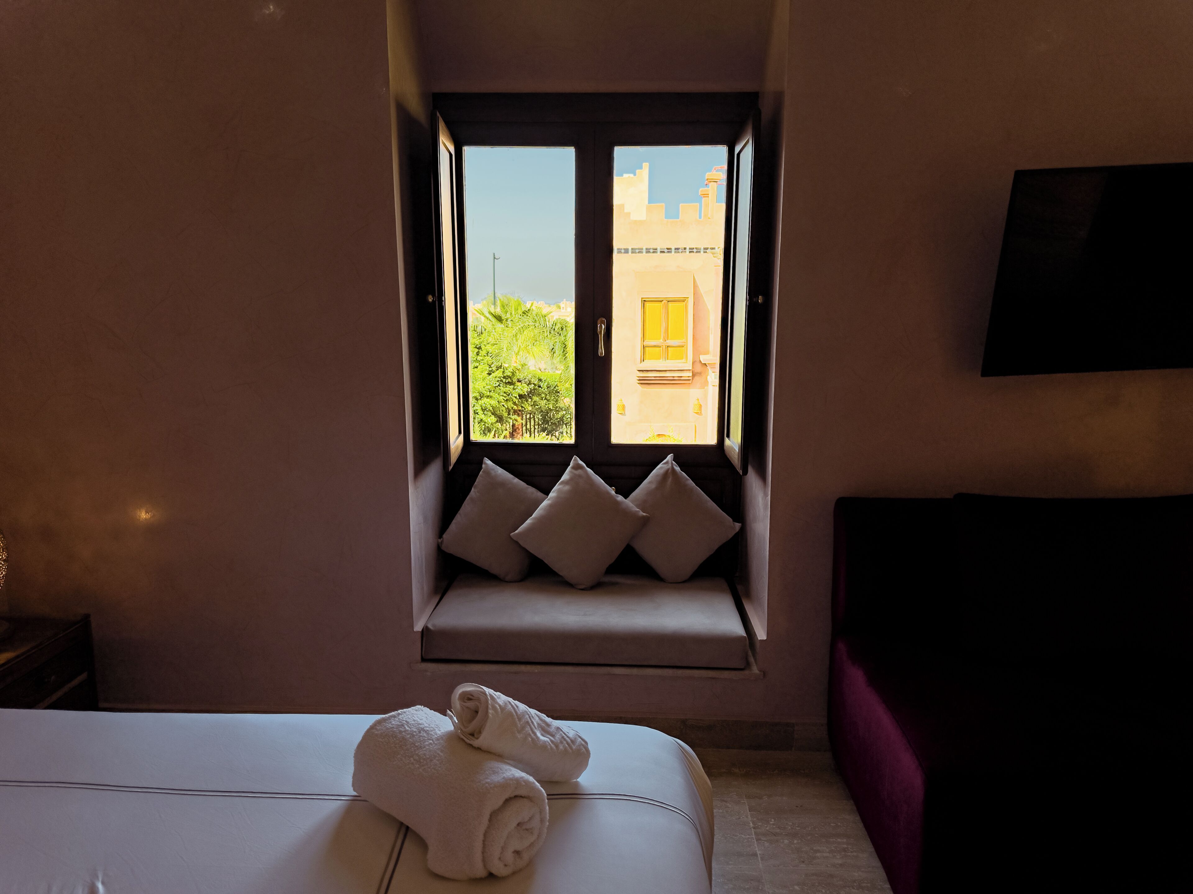 Habitación de hotel con cama, ventana con vista a edificios y televisión de pantalla plana montada en la pared.