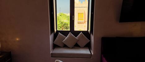 Habitación de hotel con cama, ventana con vista a edificios y televisión de pantalla plana montada en la pared.