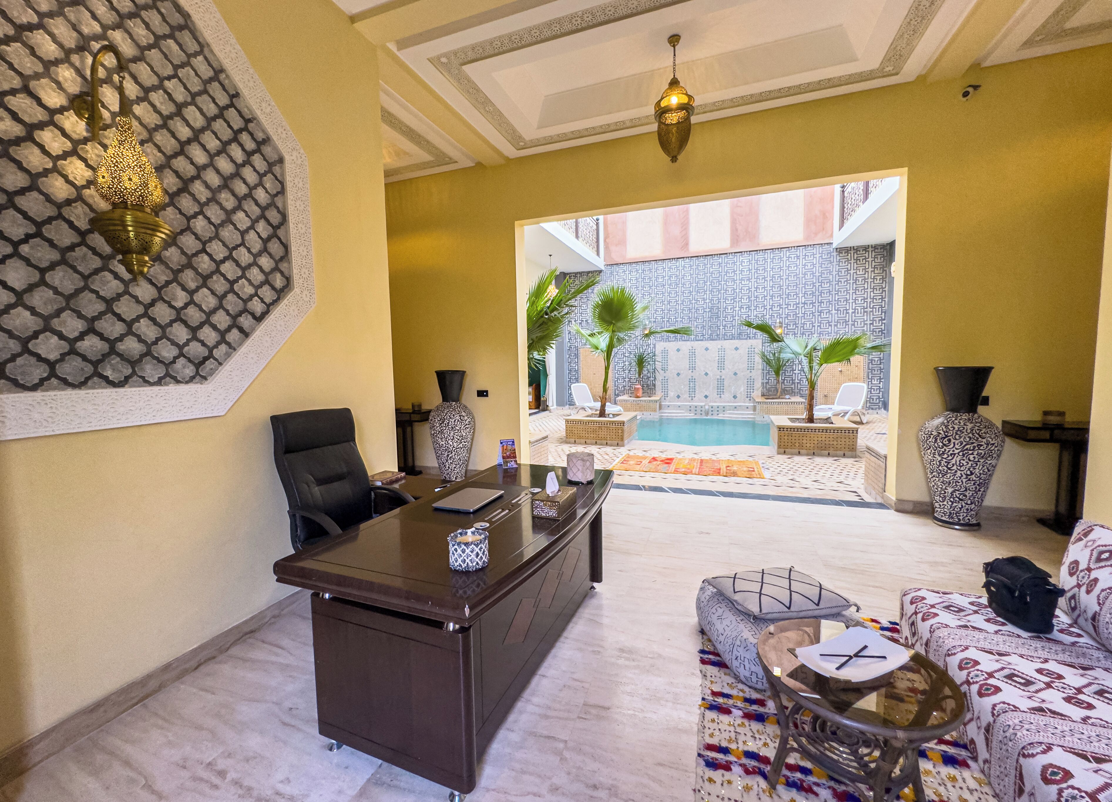 A spacious living area with a desk, comfortable seating, a large vase, and a view of an outdoor pool area.