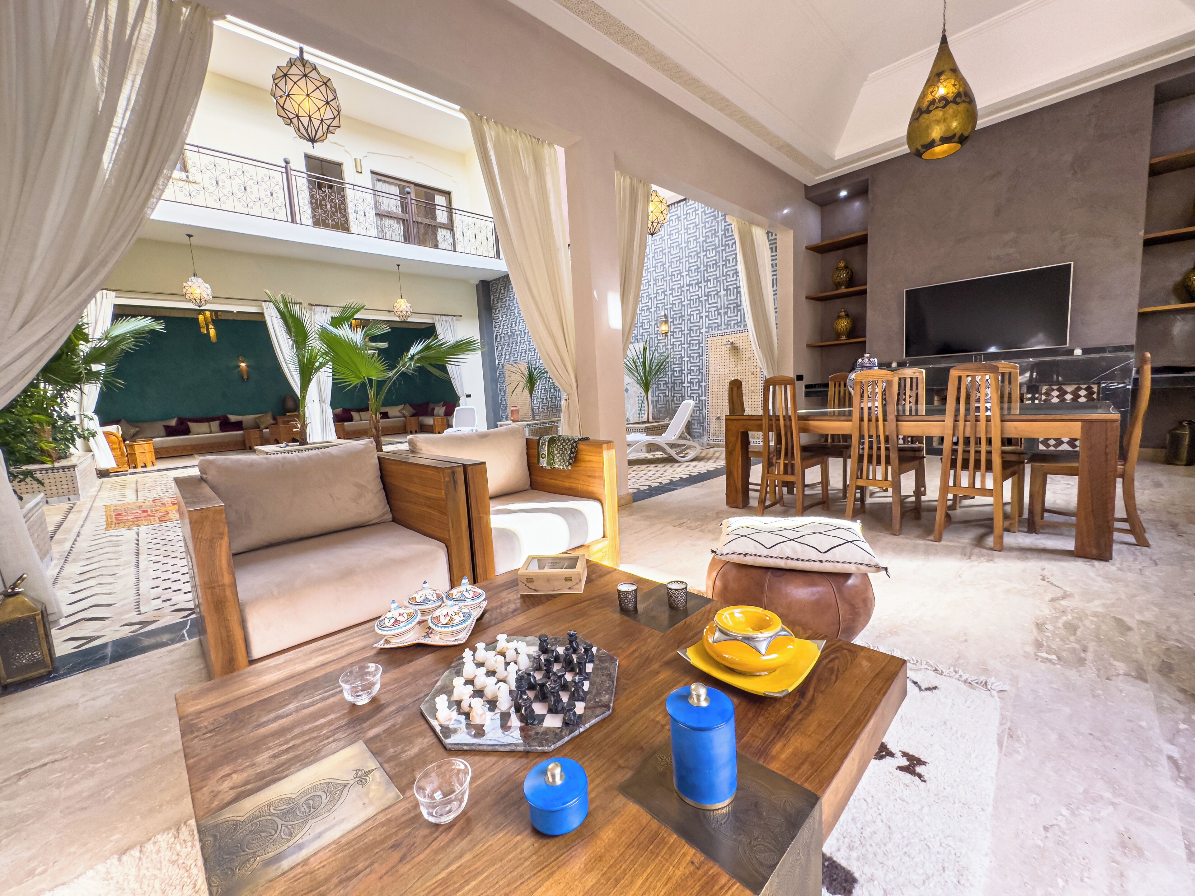 A spacious living area with a sofa, dining table, and chairs. There is a balcony with a railing and plants.