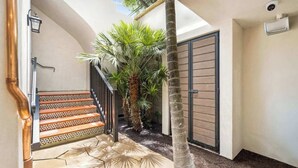 A staircase with patterned tiles leading to a door, surrounded by palm trees and a tiled patio area. - Casa Riviera 1 - Boutique Suites (Santa Barbara)