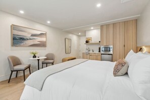 Una habitación de hotel moderna con una cama grande, un escritorio pequeño, una silla, una mesa redonda con una planta, un microondas y un armario de madera.