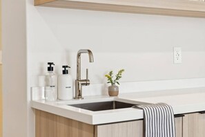 Una cocina moderna con un lavamanos de acero inoxidable, encimera blanca y armarios de madera.