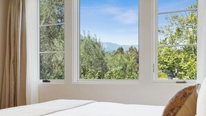 A bedroom with a large window offering a view of a forest and mountains. - Casa Riviera 6 - Boutique Suites (Santa Barbara)