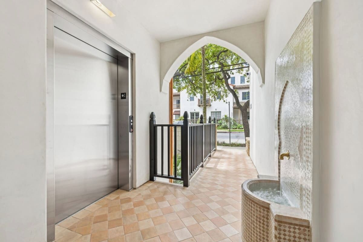 A corridor with a tiled floor, an elevator, a black metal gate, and a water feature.