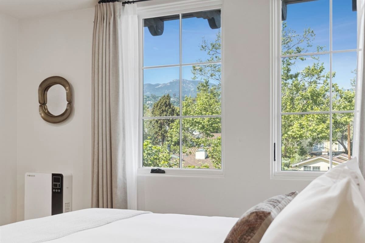 A bedroom with a large window, a bed, a radiator, and a wall-mounted mirror.