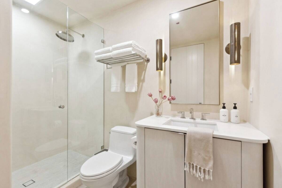 A modern bathroom with a glass-enclosed shower, a white toilet, a vanity with a mirror, and a towel rack.