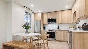 Une cuisine moderne avec des meubles en bois, des appareils en acier inoxydable et une table de salle à manger ronde, assortie de chaises.