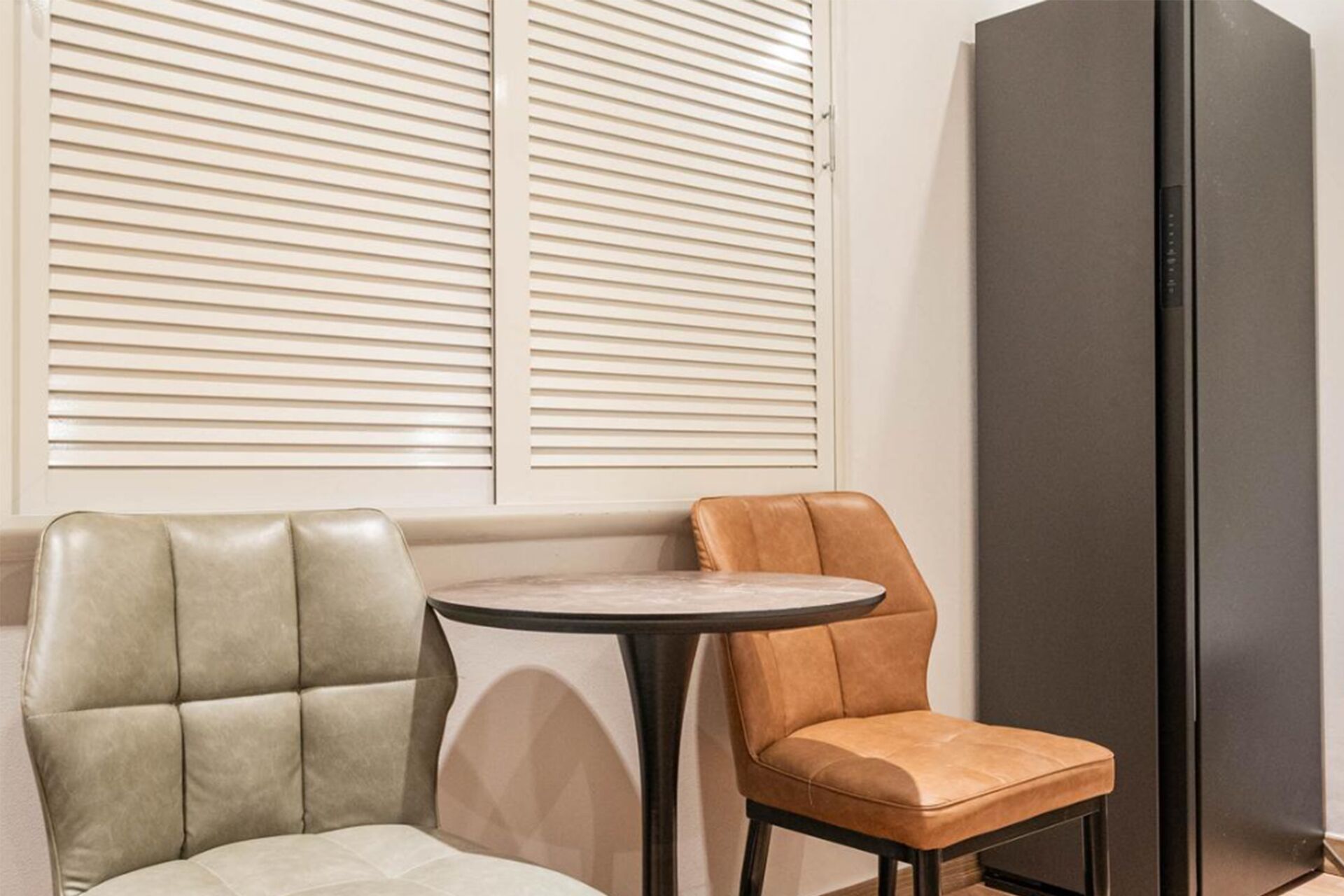 Two chairs and a table in a room with a large black cabinet and a window with blinds.
