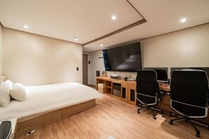 A modern bedroom with a bed, a desk with two chairs, a large TV, and a wooden floor. - ANYANG IT CENTRO HOTEL (Anyang)