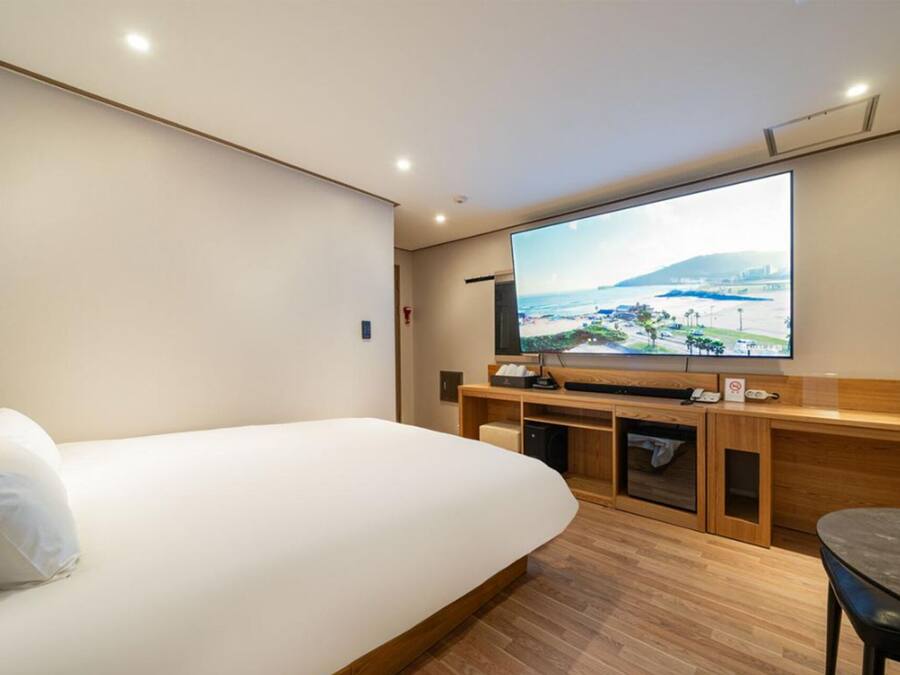 A hotel room with a bed, a TV mounted on the wall, a wooden desk, and a small table.