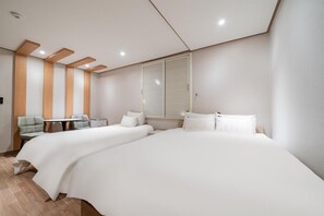 Ein modernes Hotelzimmer mit zwei Betten, einem kleinen Tisch, einem Stuhl und einem Fenster mit Jalousien.