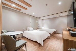 Ein Hotelzimmer mit zwei Betten, einem Schreibtisch, einem Sessel, einem Fernseher und einem Fenster mit Jalousien.