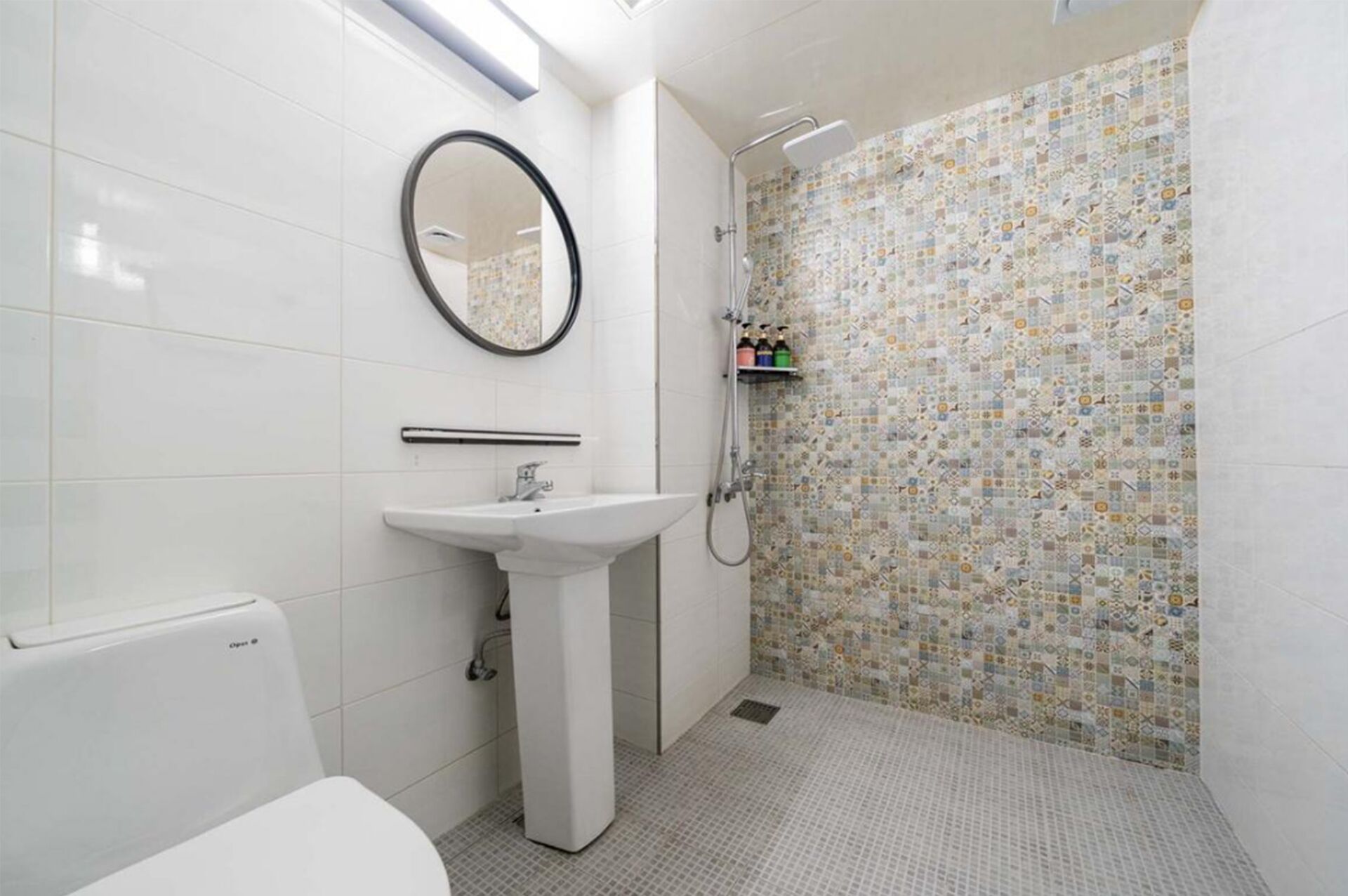 A bathroom with a white sink, a mirror, a shower with a tiled wall, and a toilet.
