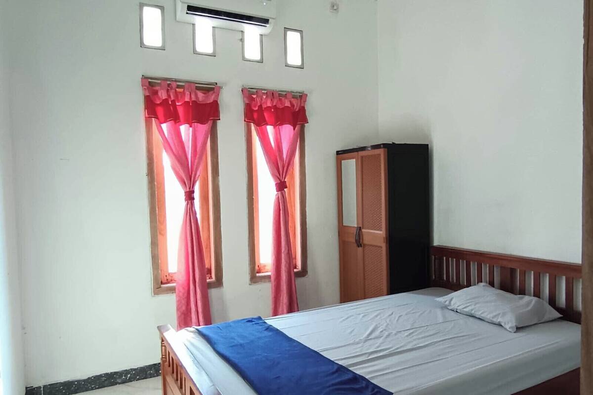 Un dormitorio con cama, armario y dos ventanas con cortinas.