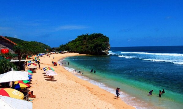 A beach with clear turquoise water, a sandy shore, and a small island with greenery. - Omah Warih Homestay (Wonosari)