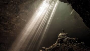 A person standing on a rock formation with a light shining through a cave opening.