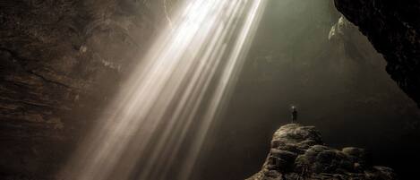 A person standing on a rock formation with a light shining through a cave opening.