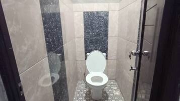 Un baño pequeño y estrecho con inodoro, zona de ducha y suelo de baldosas.