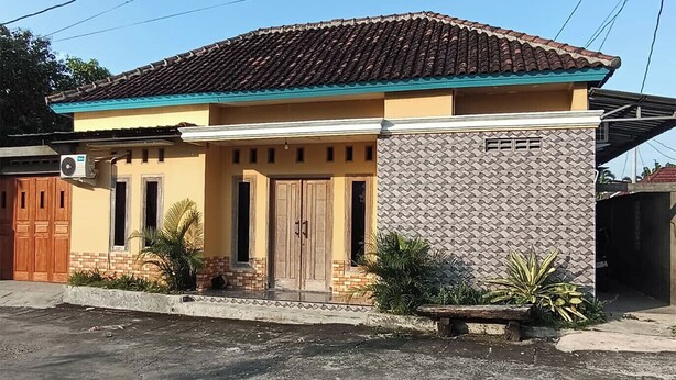 Una casa de una planta con techo de tejas, una puerta principal y un pequeño porche con plantas.