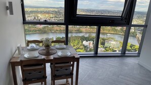 Un coin repas avec une table dressée pour quatre personnes, offrant une vue panoramique sur un lac et le paysage urbain.
