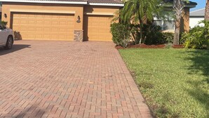 Uma casa residencial com garagem, entrada pavimentada e gramado bem cuidado com palmeiras.