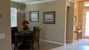 Uma sala de jantar com mesa e cadeiras, um candelabro, quadros nas paredes e um corredor que leva a outro cômodo.