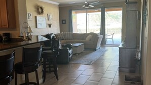 Uma cozinha espaçosa com área de jantar, uma sala de estar com sofá e cadeiras, e uma grande porta de vidro deslizante que dá para um pátio externo.
