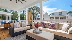 A covered outdoor seating area with a sofa and ottoman, a small table with a vase, and a view of neighboring houses. - 4BR Home with Deck & Grill Fun + Free Attraction Tickets! (Santa Rosa Beach)