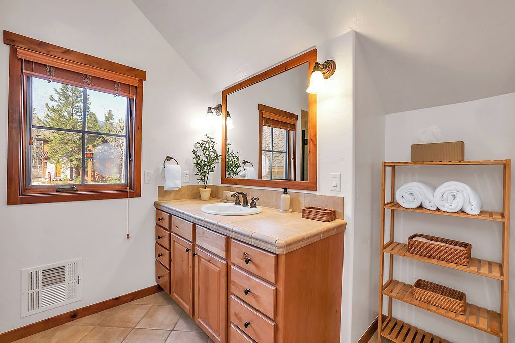 A bathroom with a wooden vanity, a large mirror, and a window with a view of trees.