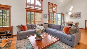 A spacious living room with a sectional sofa, a coffee table with a plant, and large windows offering a view of trees.
