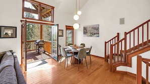 A spacious dining area with a wooden table and chairs, a grill outside, and a staircase with wooden railings.