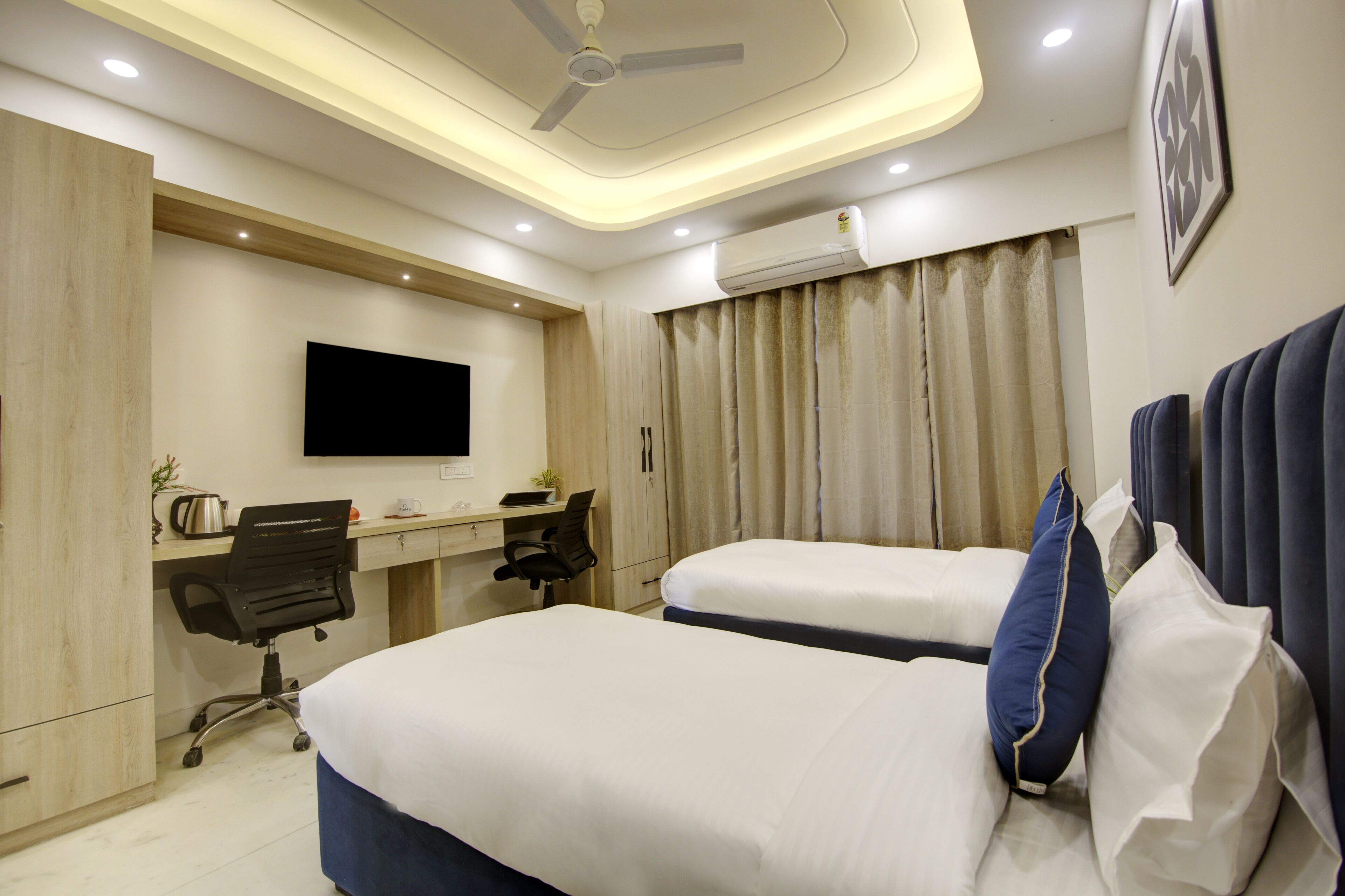 A hotel room with two beds, a desk, a chair, a television, and an air conditioning unit.