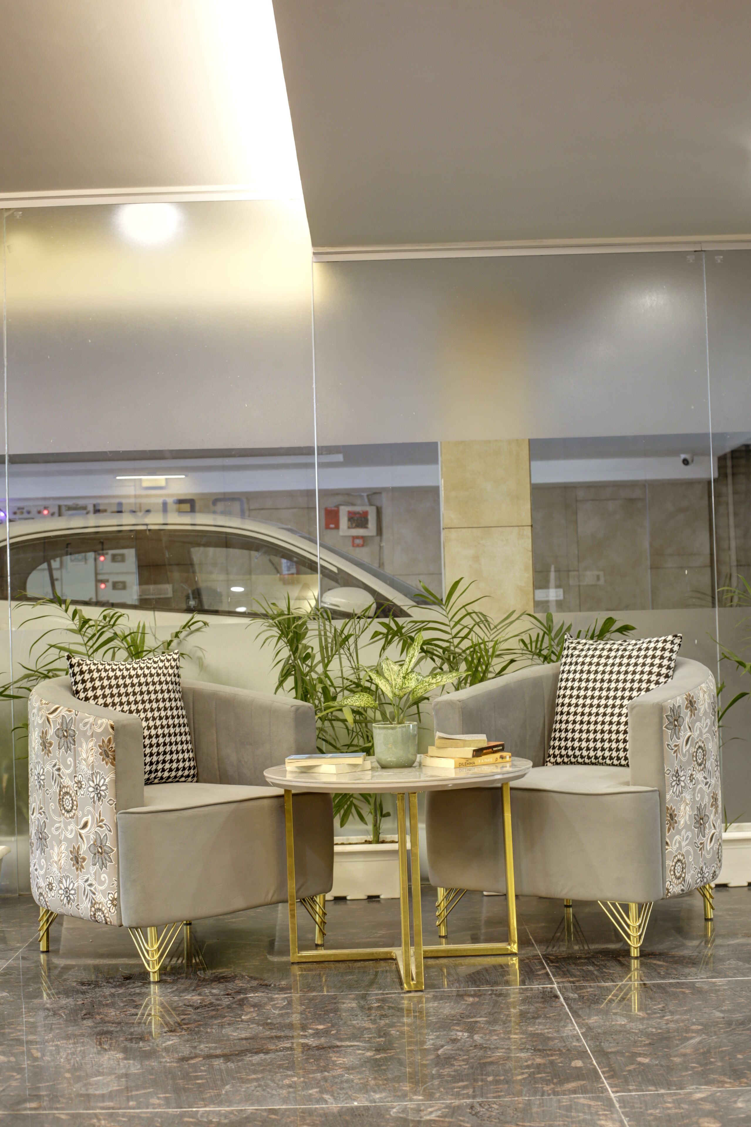 En moderne lobby med et siddeområde, to sofaer med mønstrede hynder, et lille rundt bord med bøger og en potteplante.